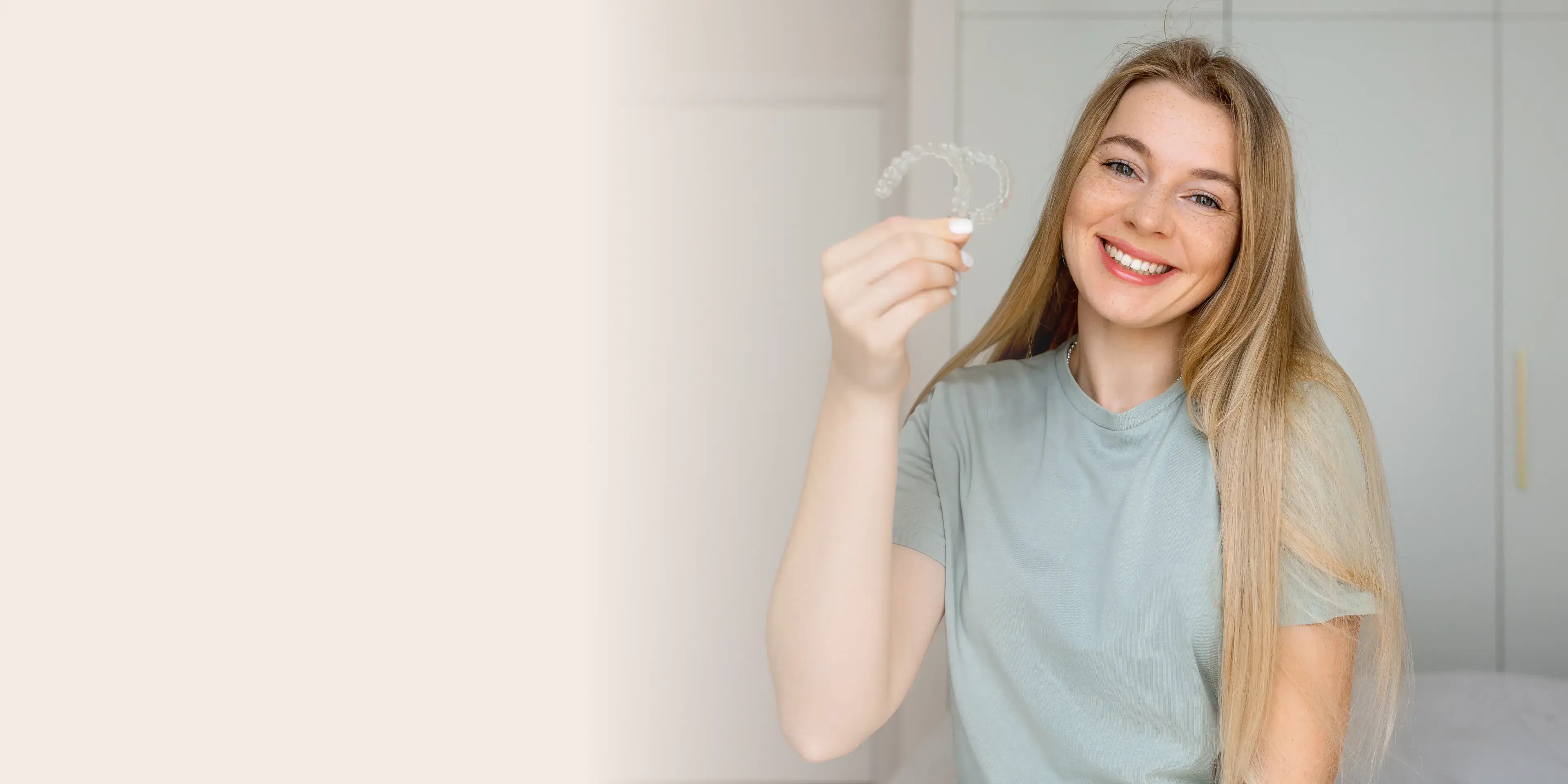 Smiling woman with long blonde hair holding clear dental aligners.