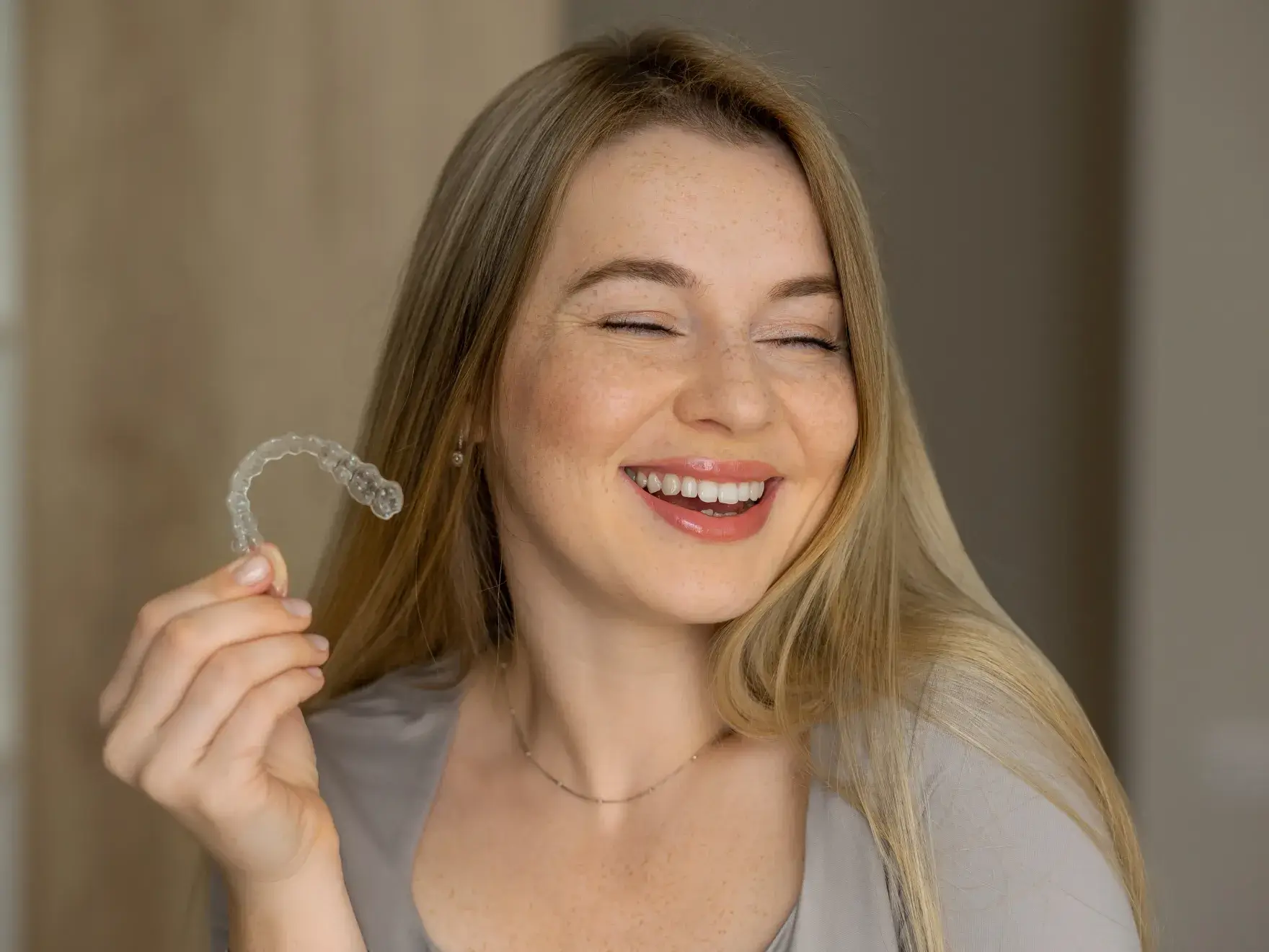 Smiling woman with long blonde hair holding a clear dental aligner.