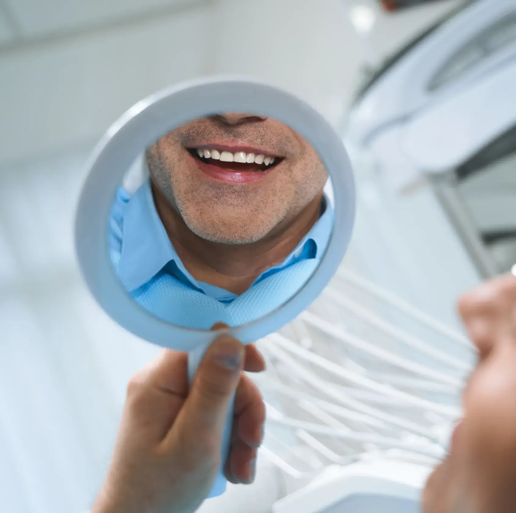Man smiling and looking at his teeth in a handheld mirror at a dental clinic.