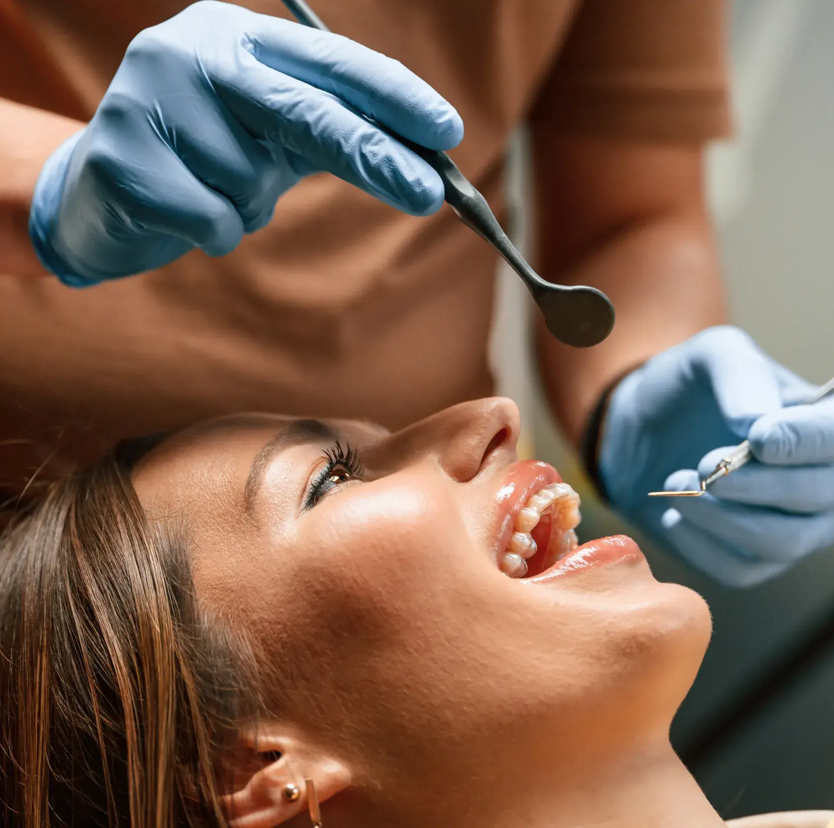 Close-up of a smiling woman at a dental appointment with a dentist wearing blue gloves holding dental tools.