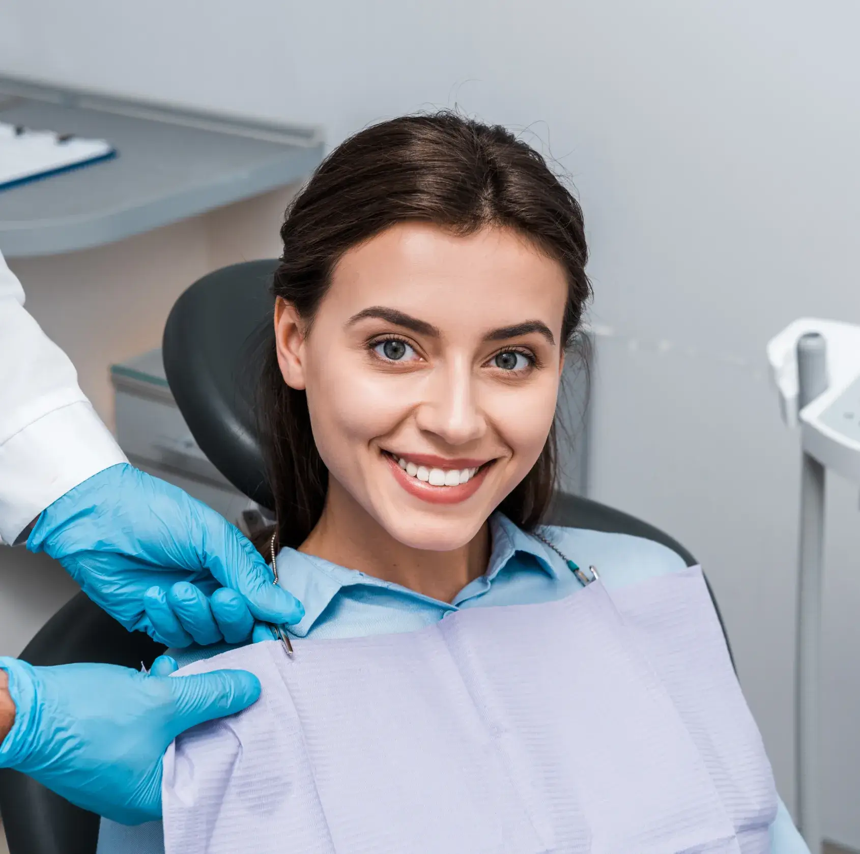Smiling woman sitting in a dental chair as a dentist places a protective bib around her neck.