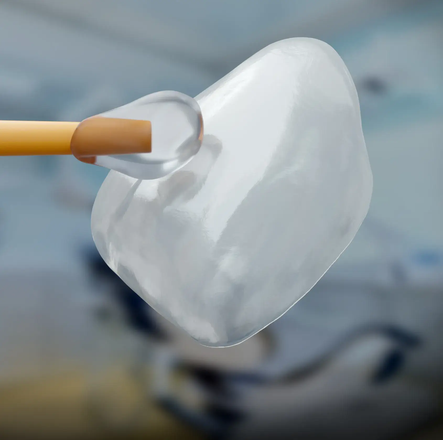 Close-up of a dental veneer held by a tool against a blurred background.