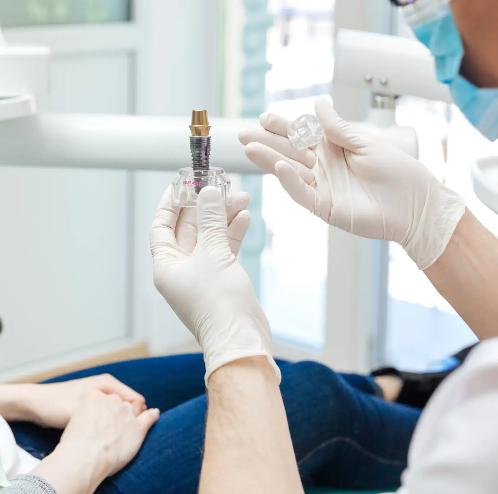 Dentist wearing gloves showing a dental implant model to a seated patient in a dental office.