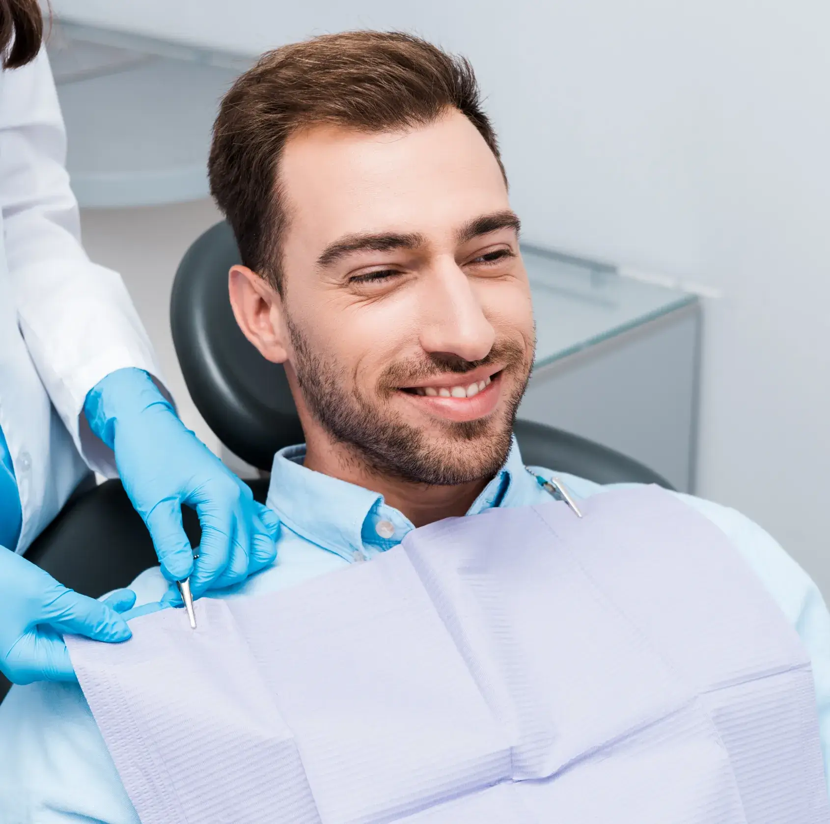 Smiling man sitting in dental chair while dentist adjusts protective bib.