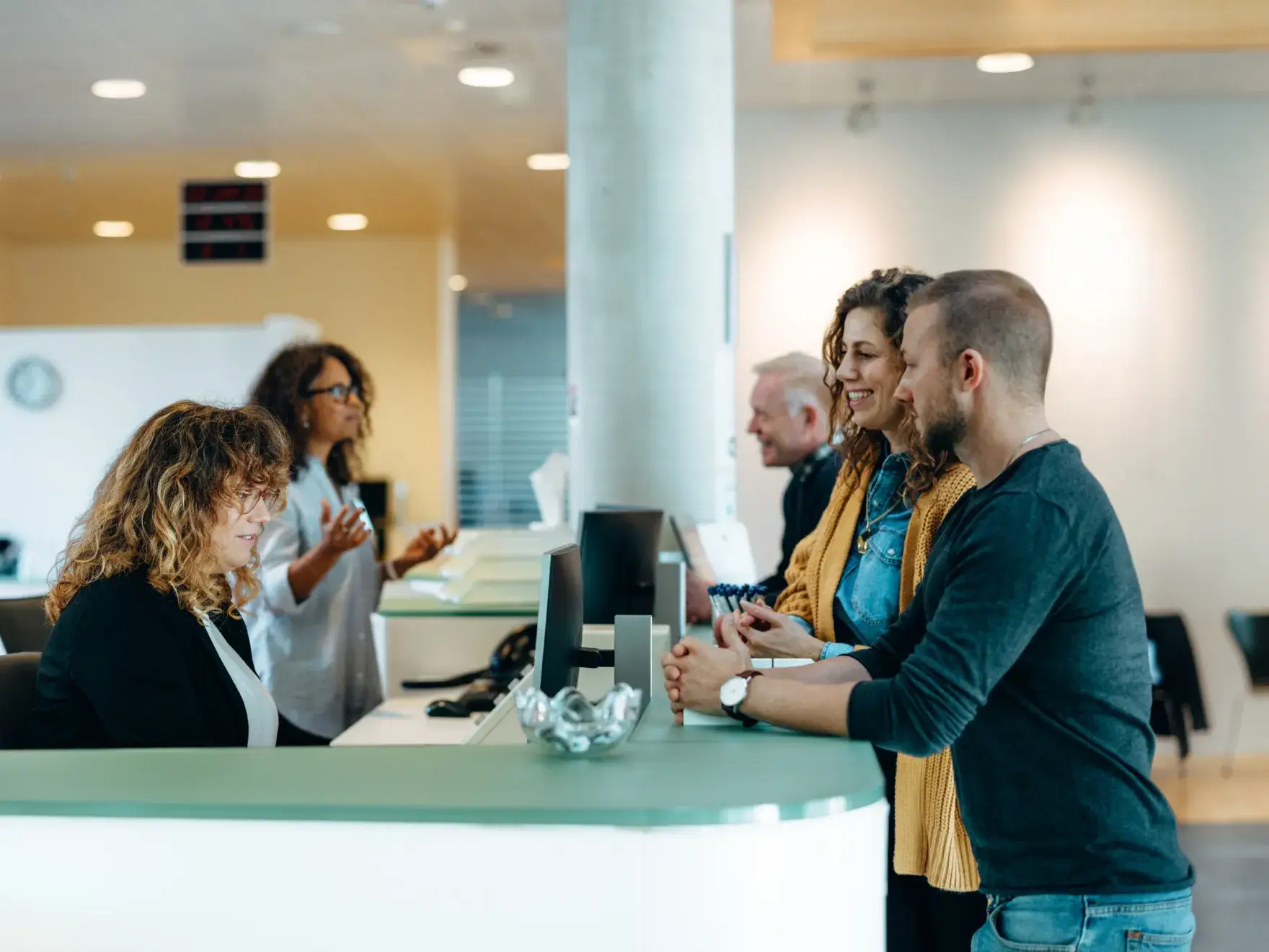 People interacting with receptionists at a modern service desk in a brightly lit office.