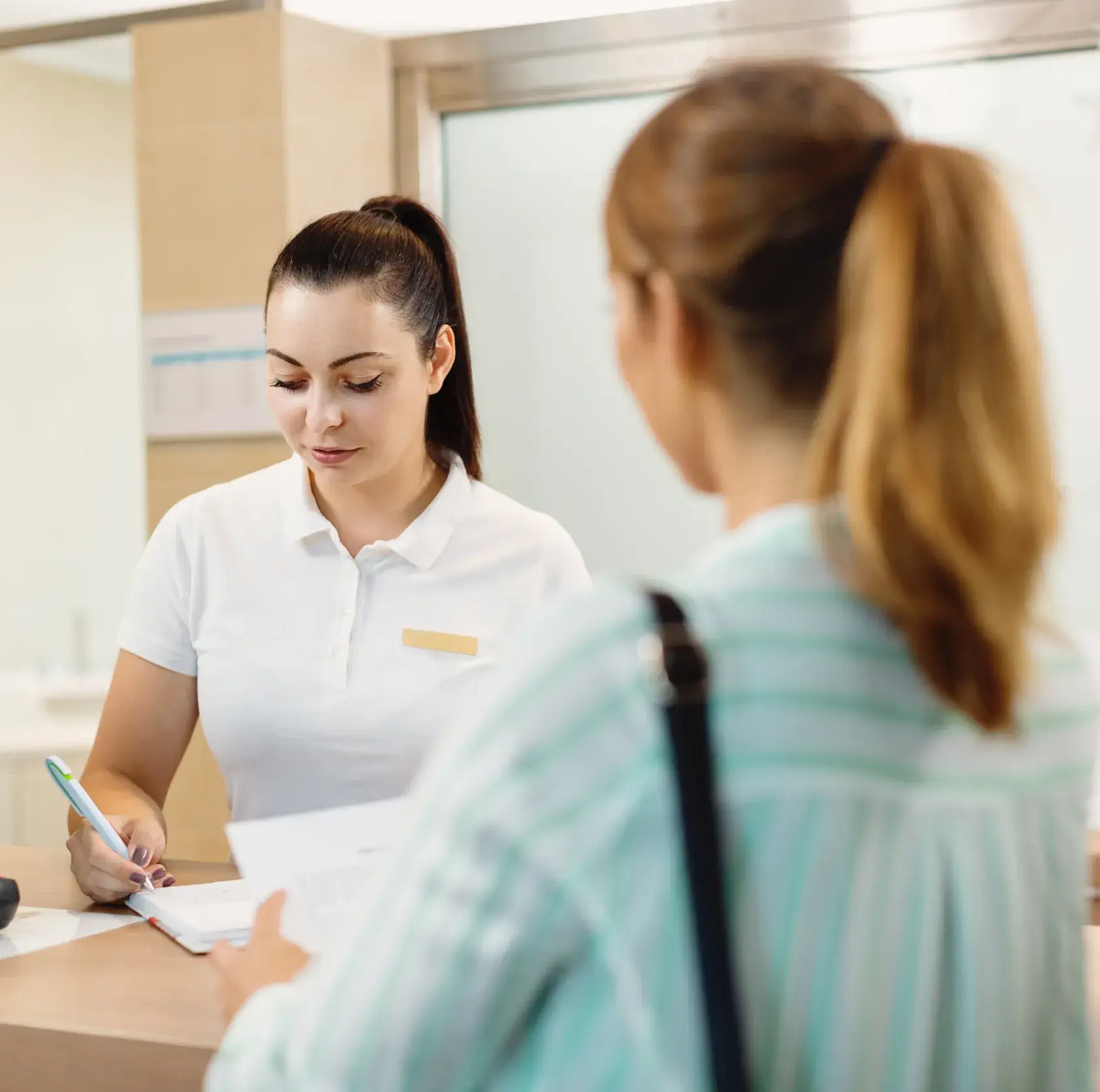 Woman with ponytail in white shirt assisting a customer holding documents at a service desk.