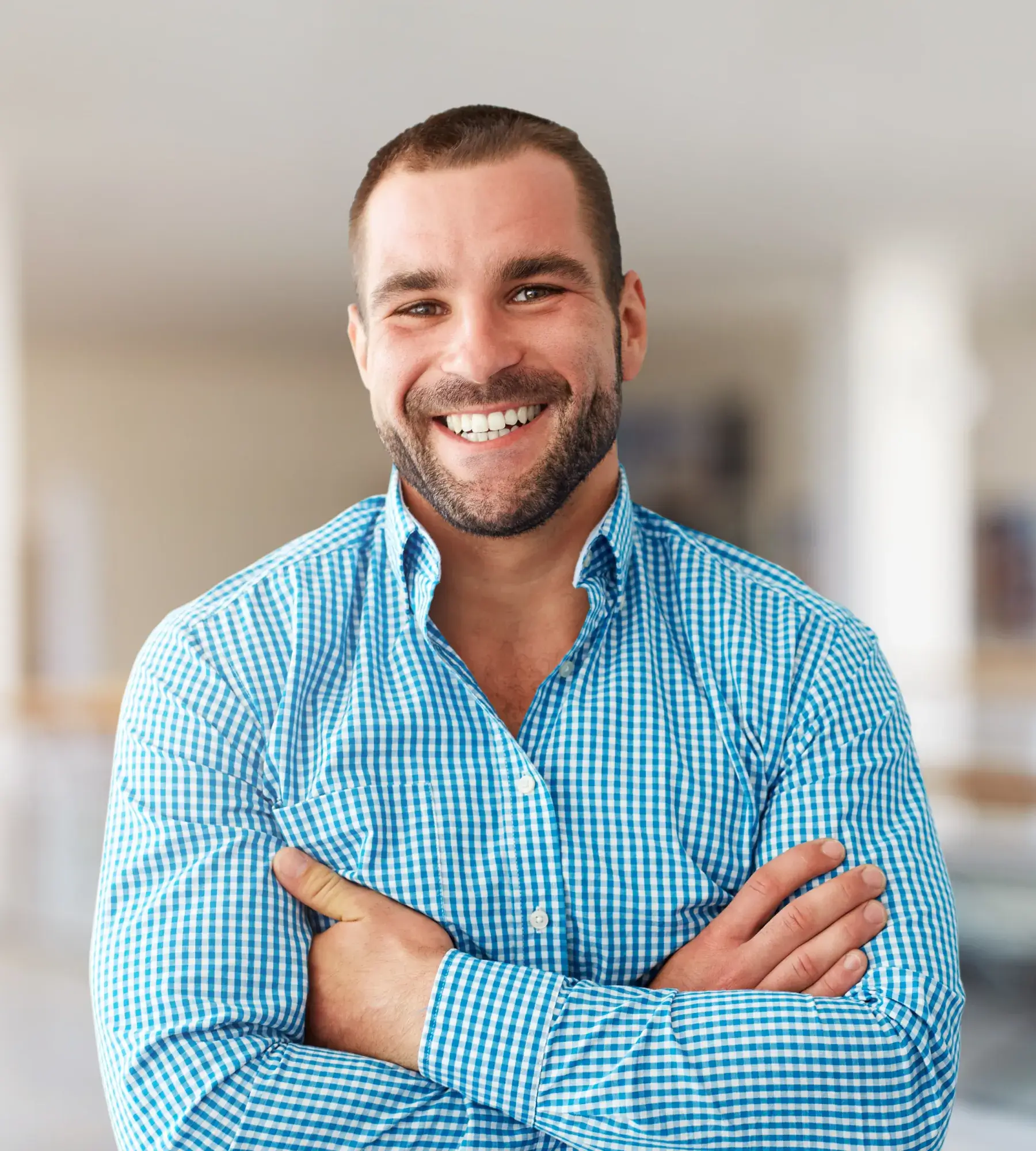 Smiling man with short hair and beard wearing a blue checkered shirt with arms crossed.