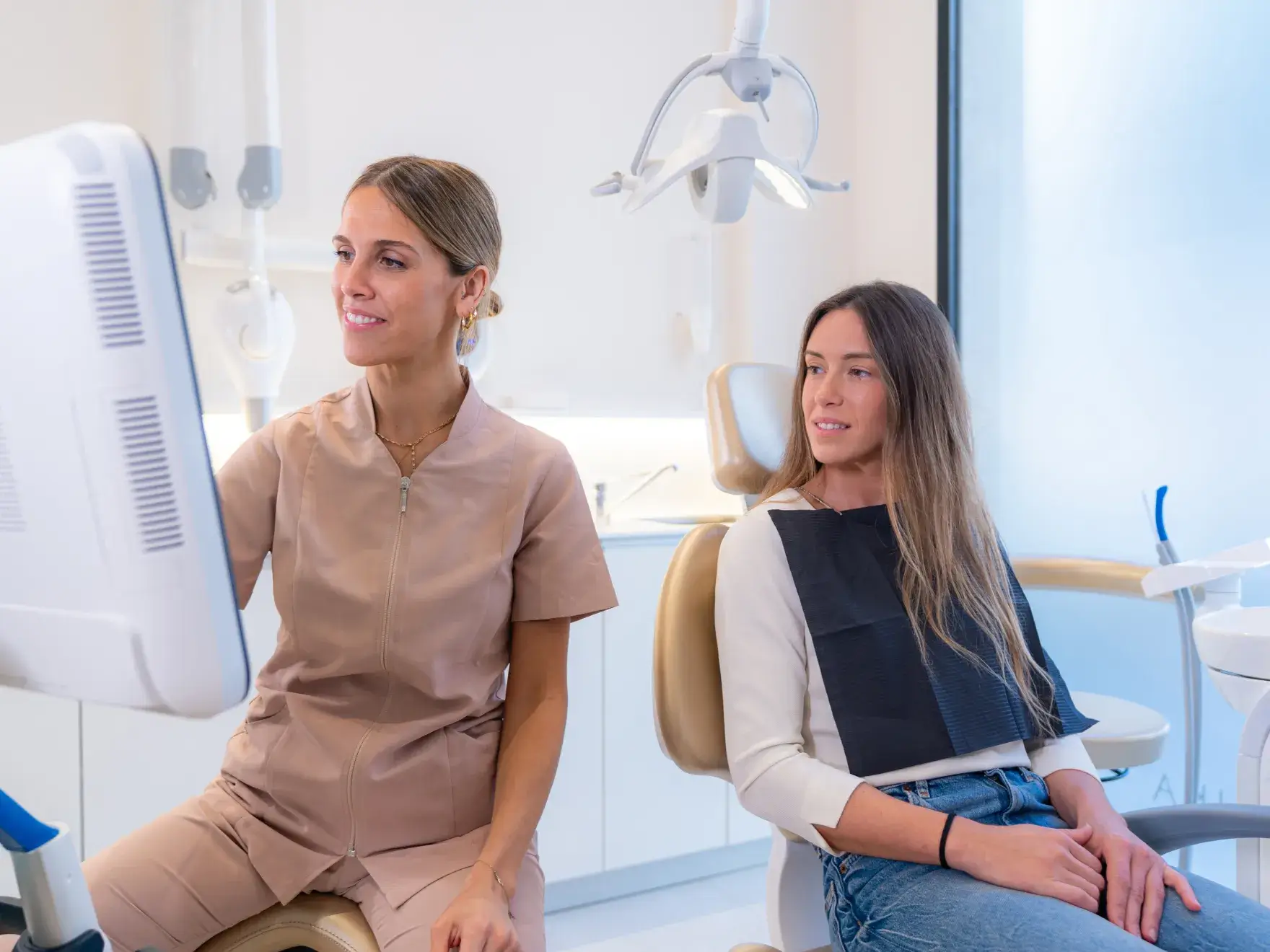 Dentist showing a digital X-ray on a screen to a female patient seated in the dental chair.