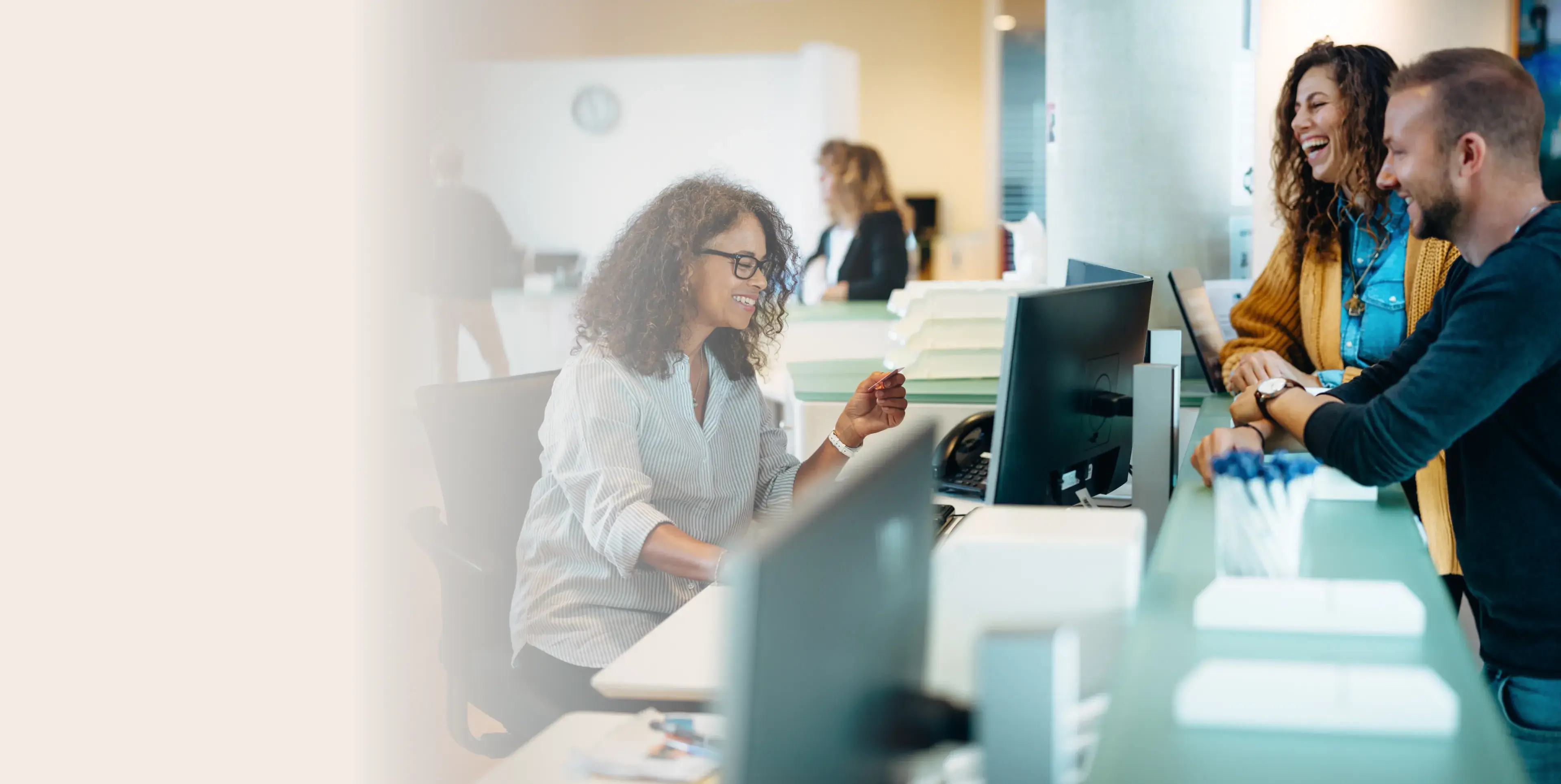 Smiling office worker assisting a man and woman at a reception desk in a bright modern office.