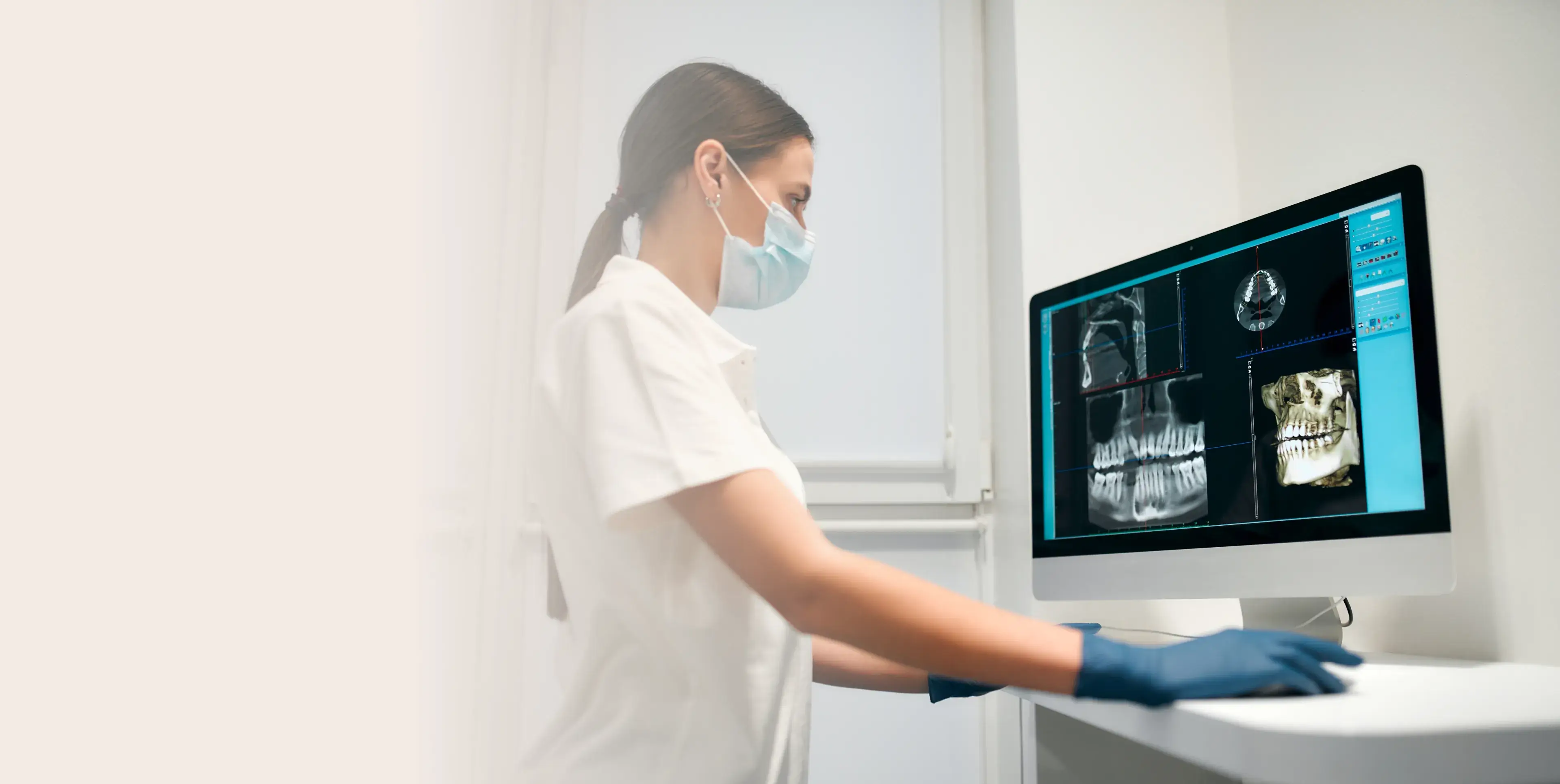 Dental professional wearing mask and gloves examining 3D dental X-ray images on computer screen.
