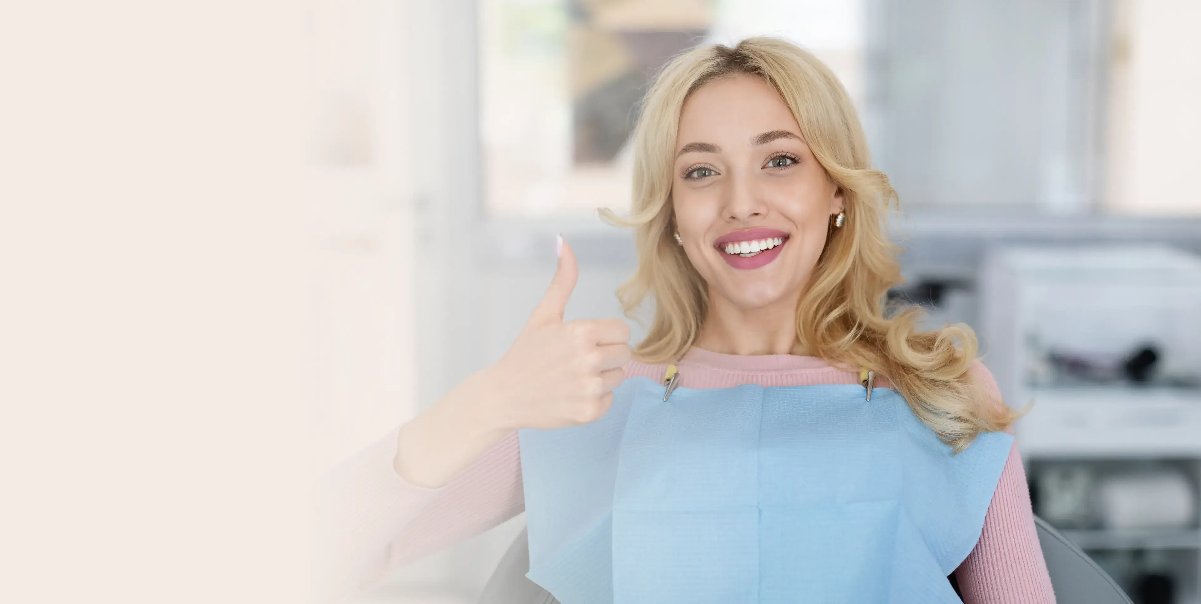 Smiling woman sitting in a dental chair giving a thumbs-up while wearing a dental bib.