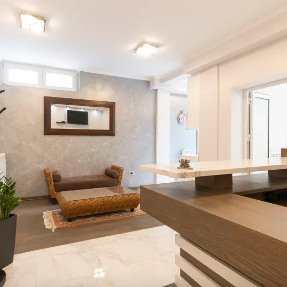 Modern living room with wicker bench, glass coffee table, wall-mounted mirror reflecting TV, and marble flooring in the foreground.