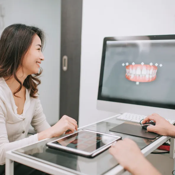 Woman consulting with a dental professional who is showing a digital 3D model of teeth on a computer screen.