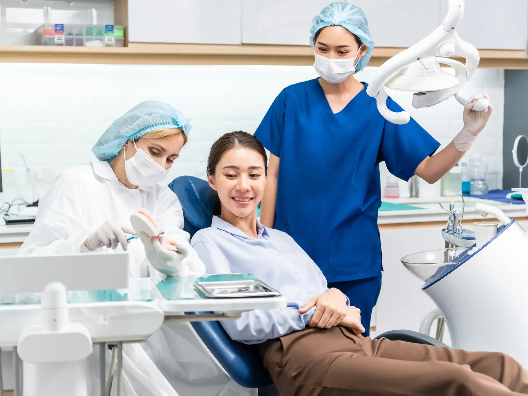 Dentist demonstrating dental care using a teeth model to a smiling patient in a dental clinic.