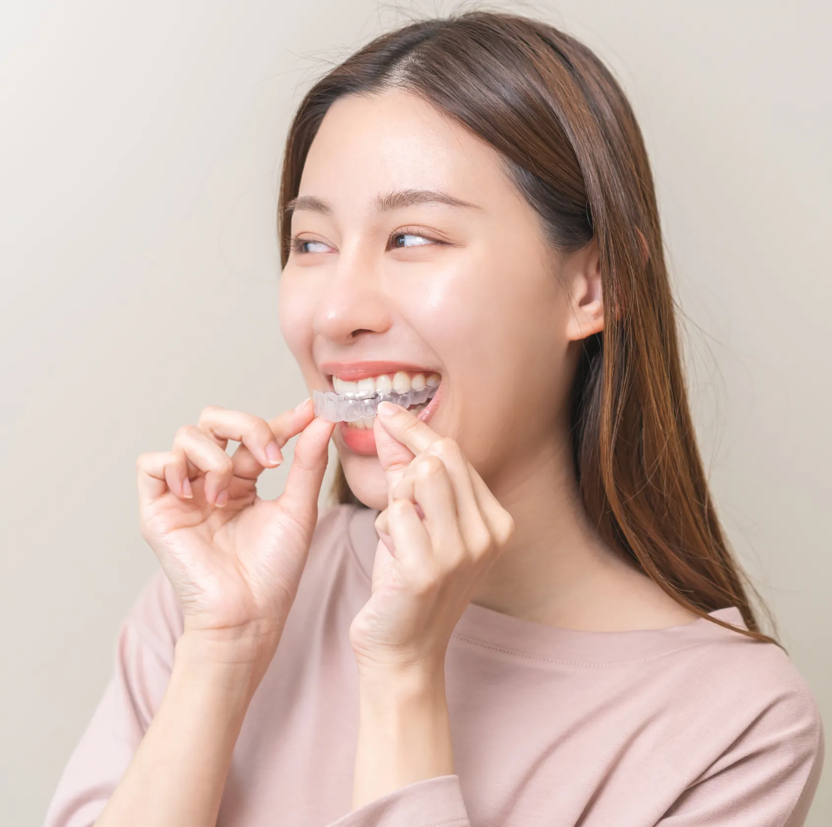 Smiling woman with long hair holding a clear dental aligner near her teeth.