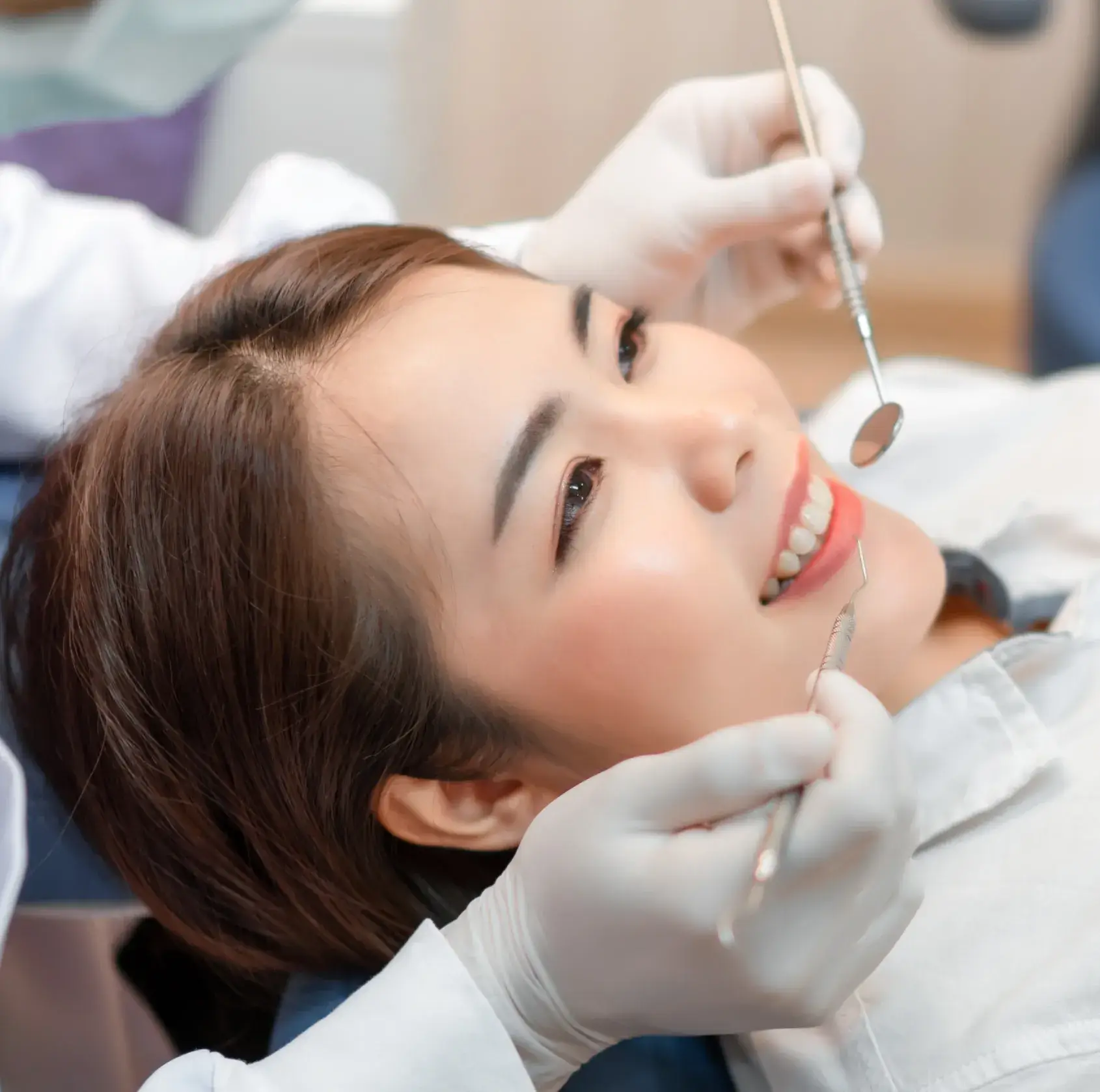 Close-up of a woman smiling while a dentist with gloved hands examines her teeth using dental tools.
