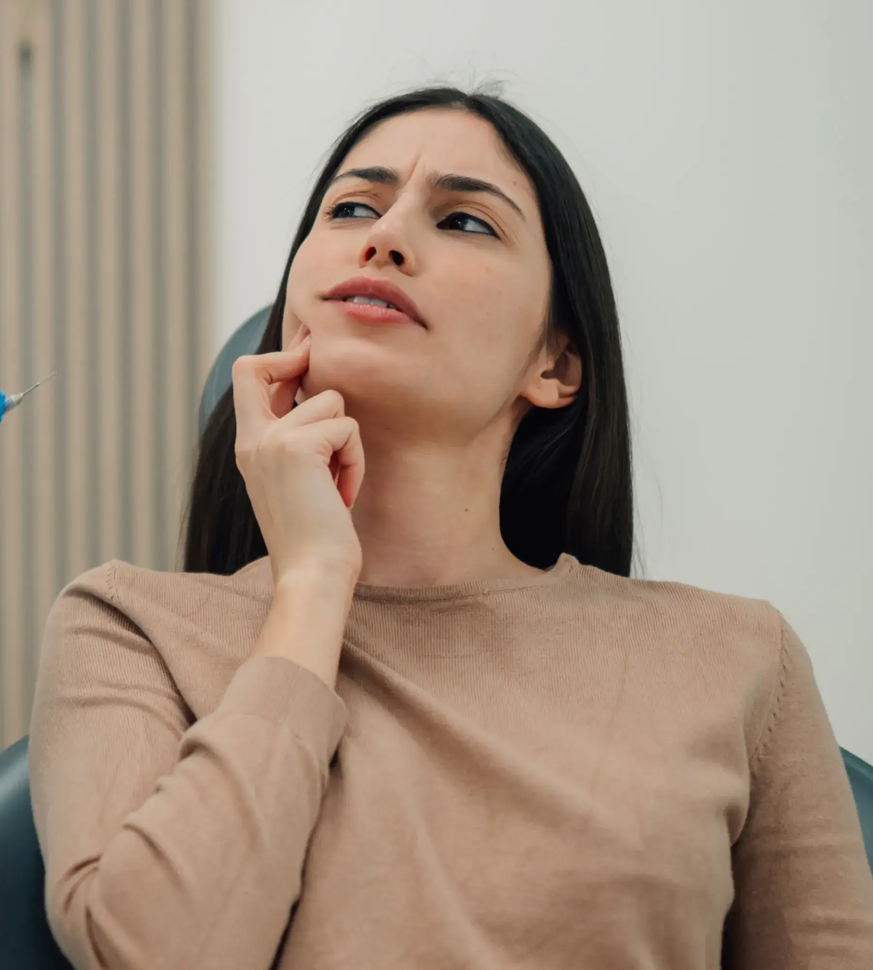 Woman in a beige sweater touching her cheek with a concerned expression, a syringe is partially visible nearby.