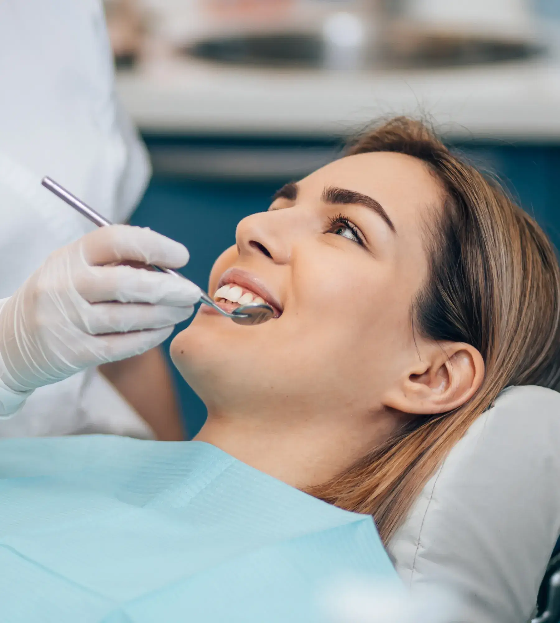 Woman reclining in dental chair with dentist’s gloved hand holding a dental mirror near her teeth.