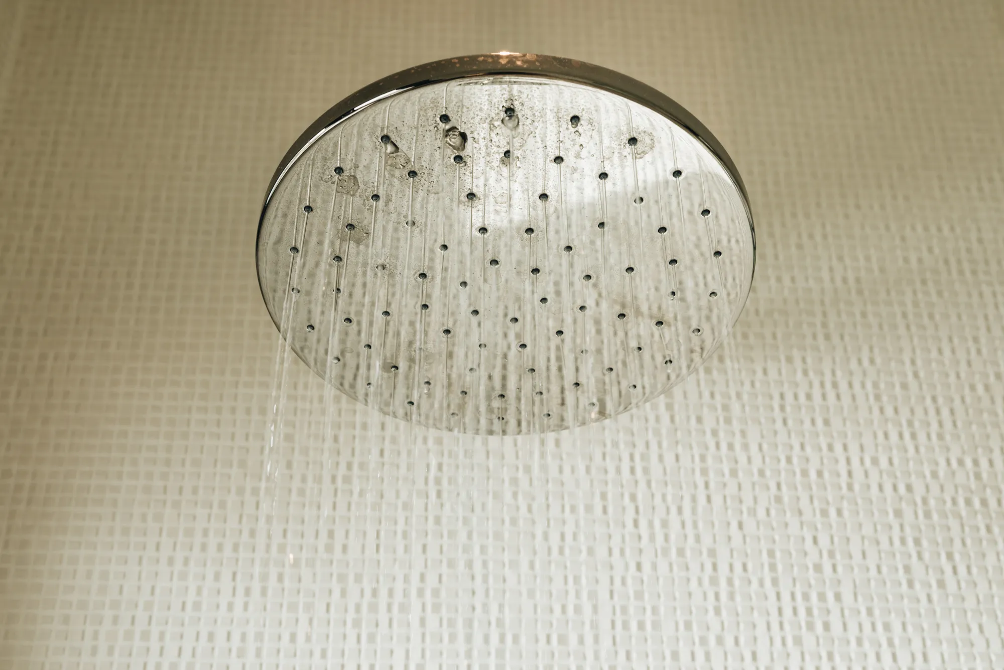 Close-up of a round silver showerhead spraying water against a white textured tile wall.