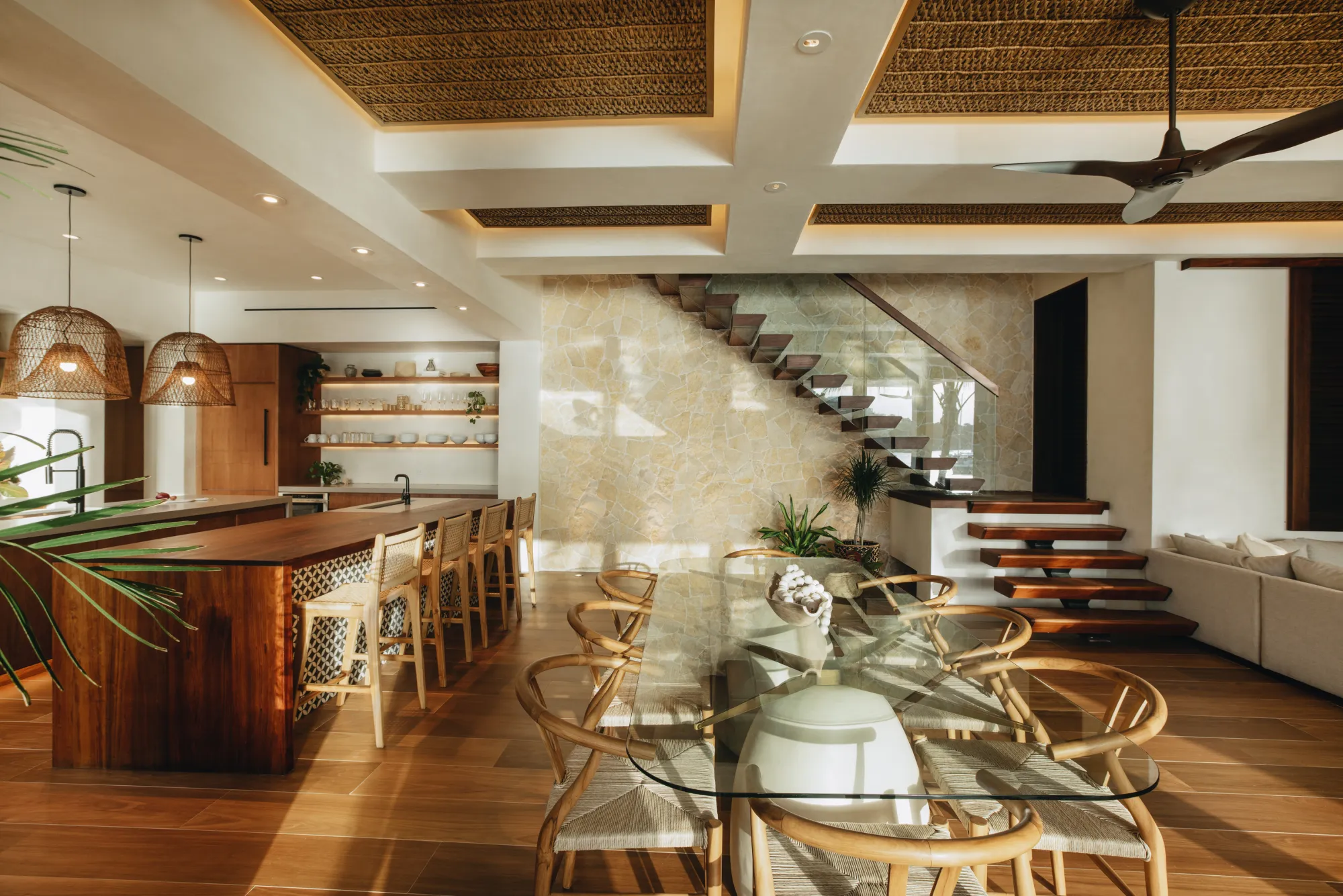 Modern two-story white house with large glass doors, balcony, and outdoor seating on a sandy ground.