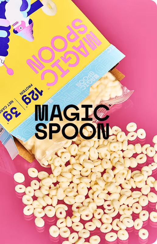 Magic Spoon cereal box tilted with cereal rings spilling onto a pink surface.