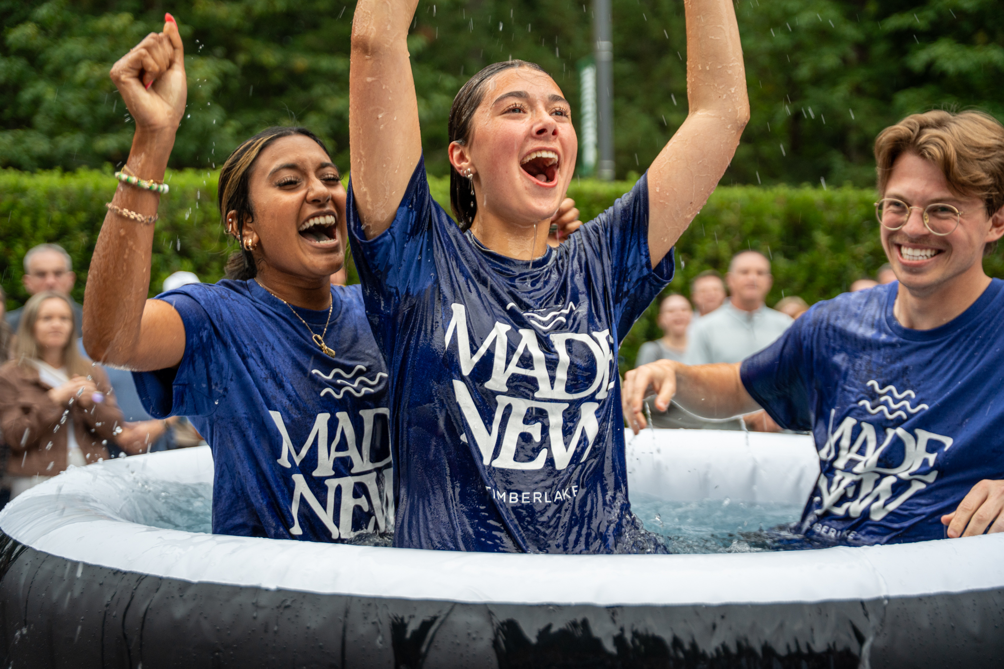 Three people in an outdoor tub for baptisms with their hands raised shouting with joy.