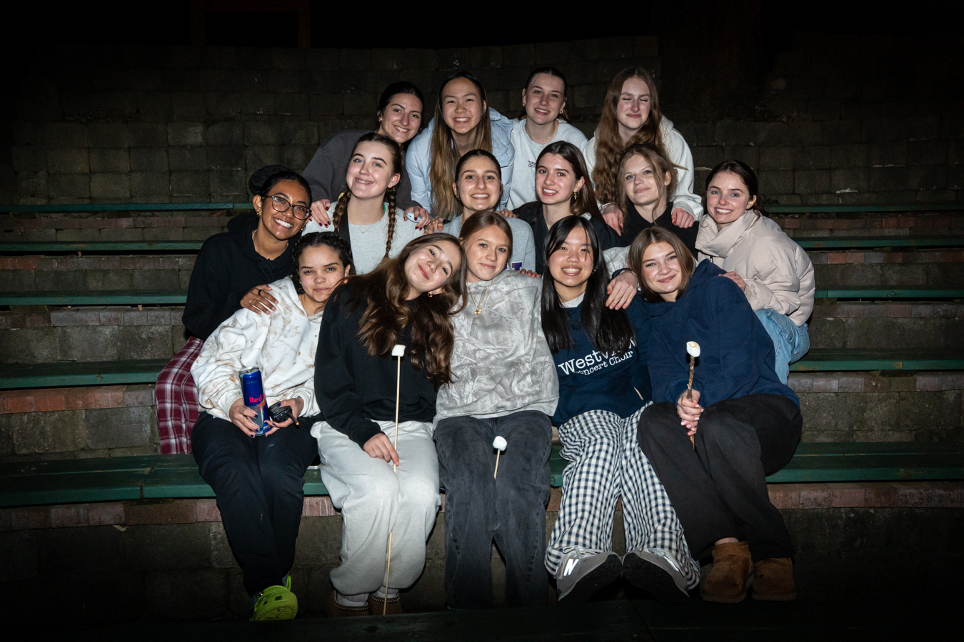 A group of girls seated outside on bleachers, smiling.