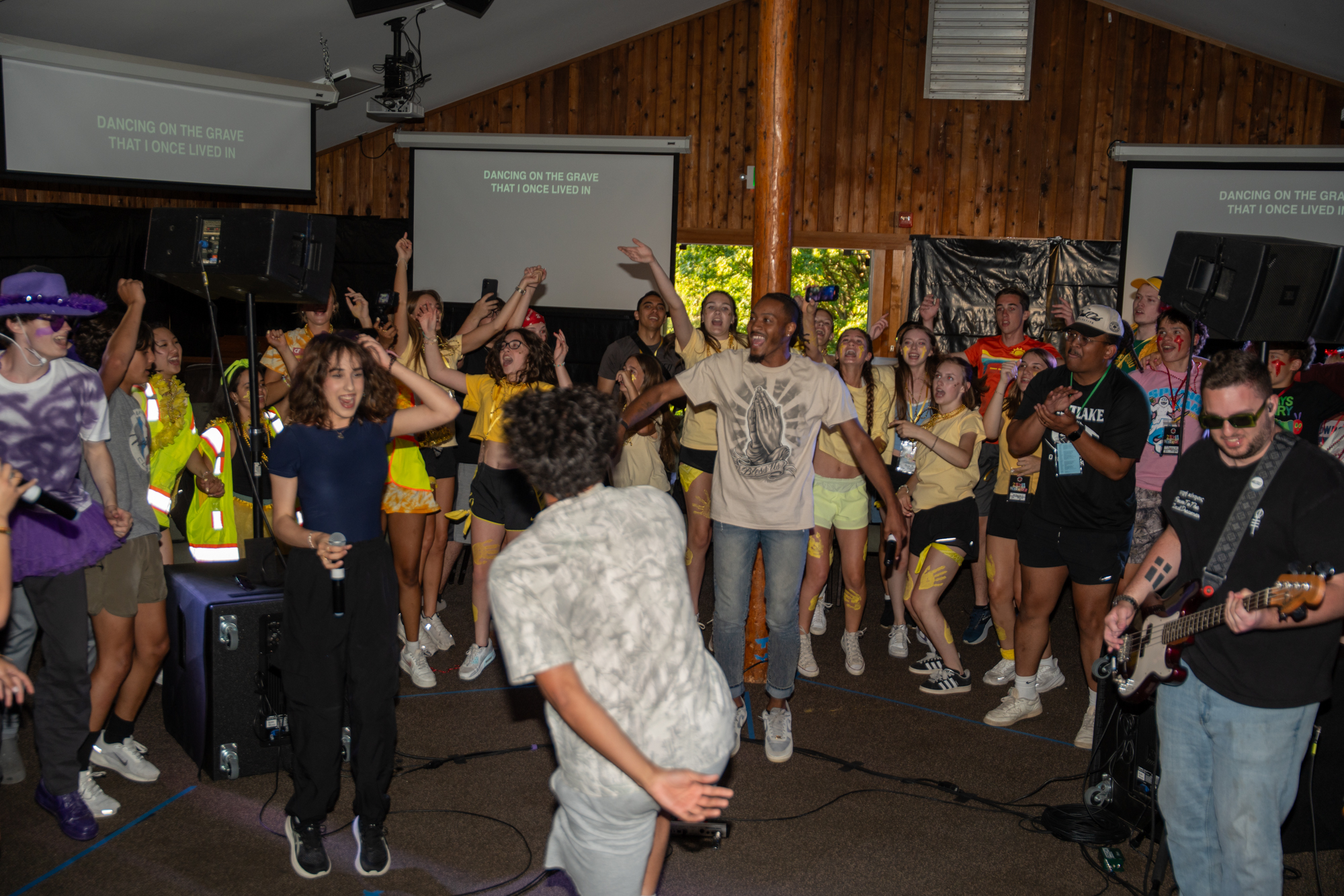 A group of students at summer camp in a circle worshiping together with hands raised.