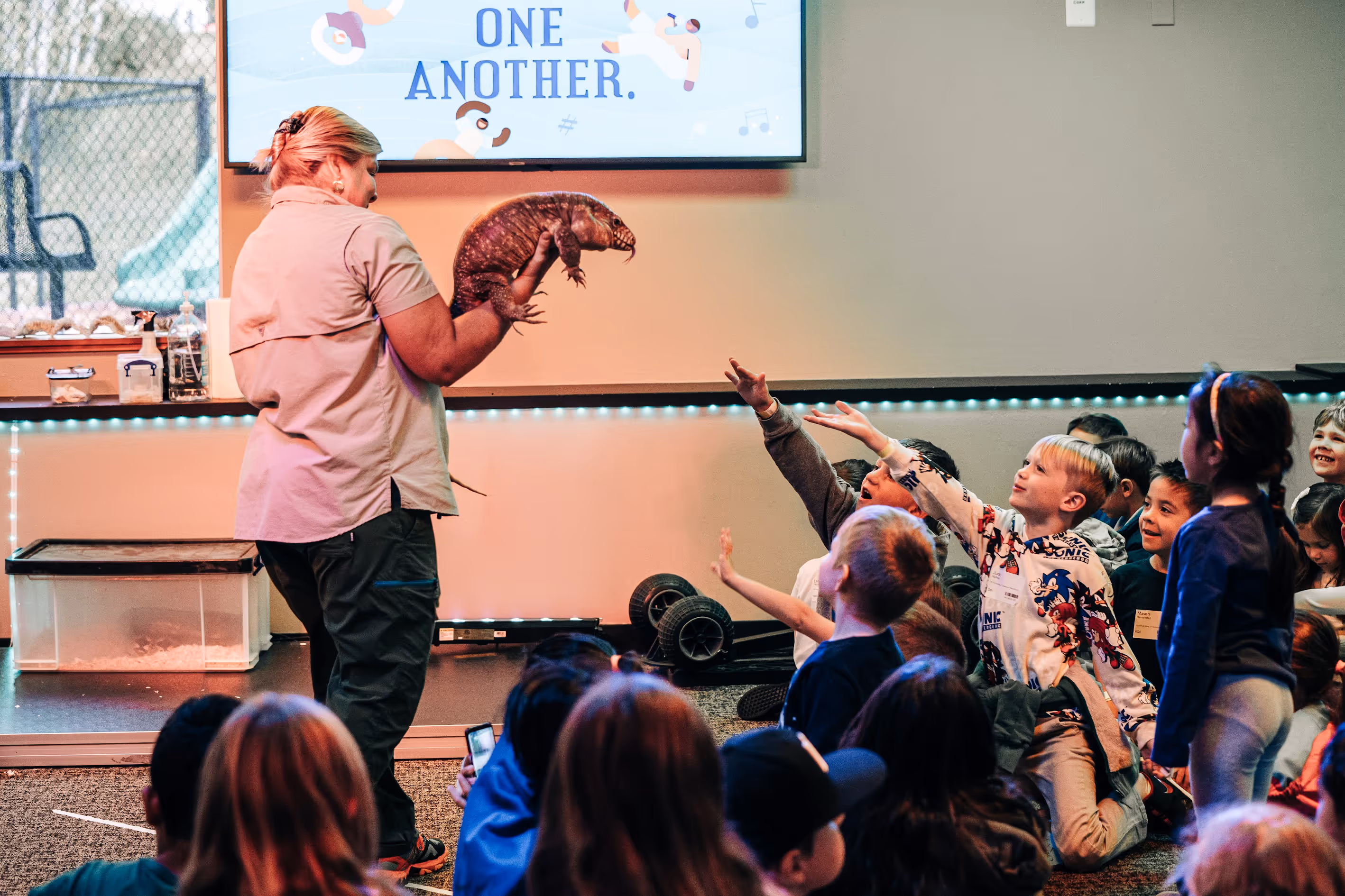 A professional holding a lizard to an audience of children.