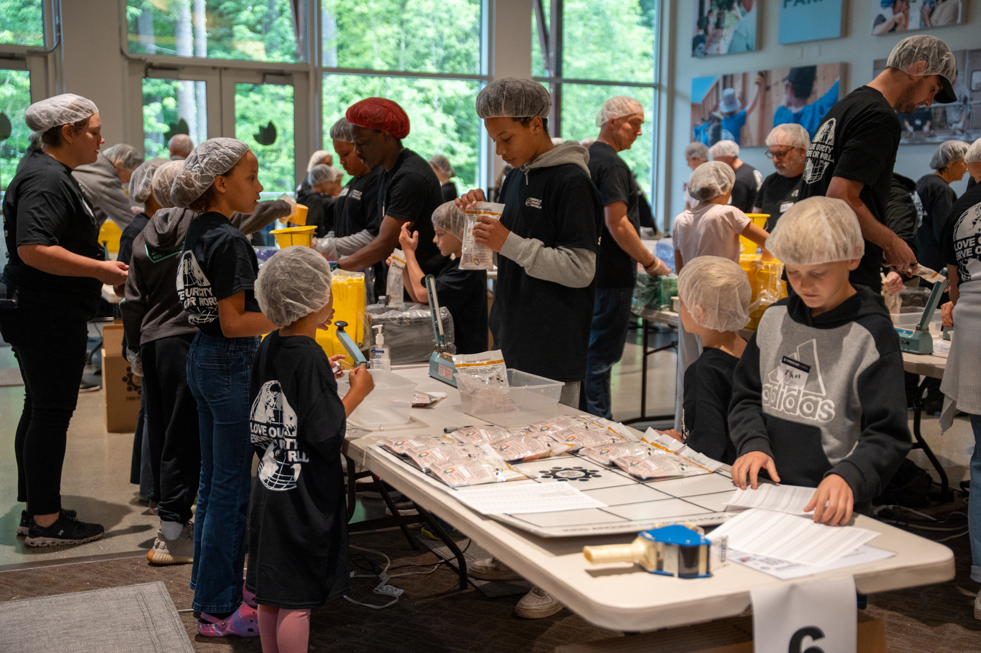 Kids and adults wearing hair nets packaging food.
