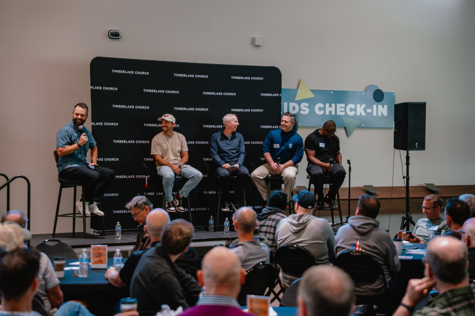 A gathering of men listening to a panel of men in the main lobby.