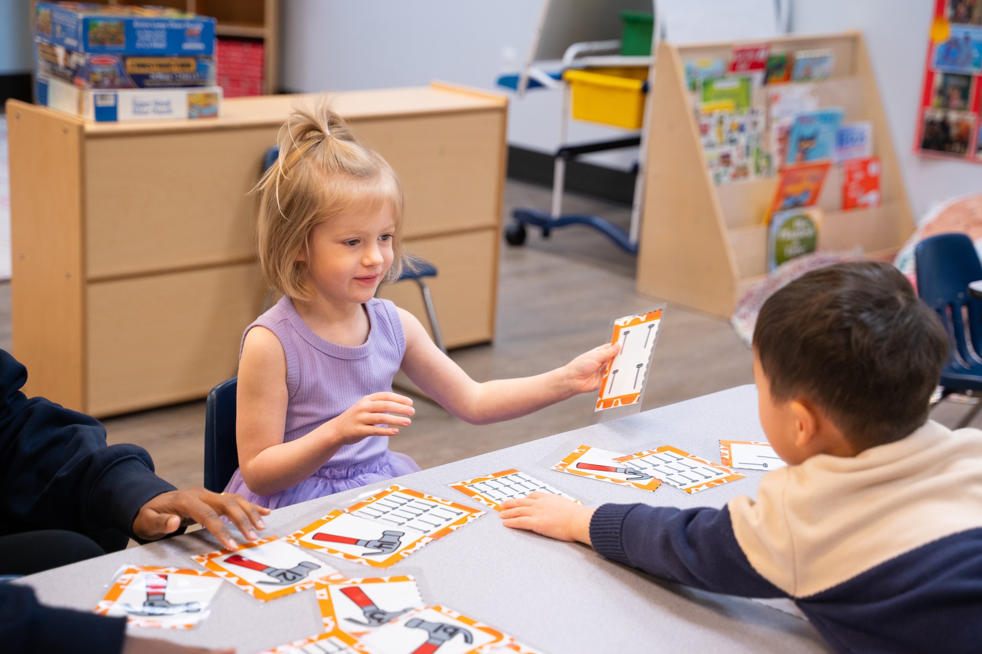 Teo preschoolers handing paper to each other across the table.