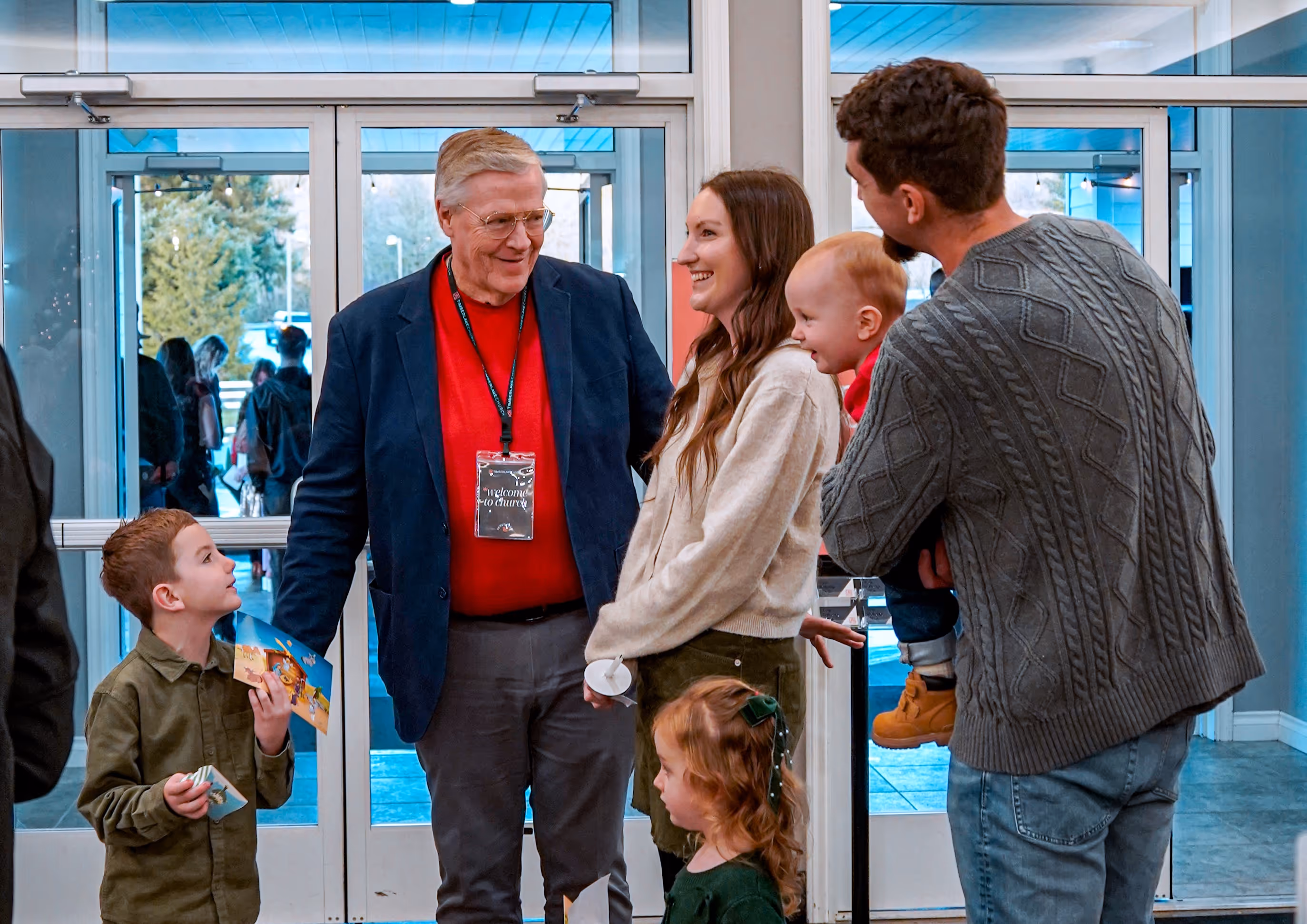 A volunteer greeting a family of five at the doors of church.