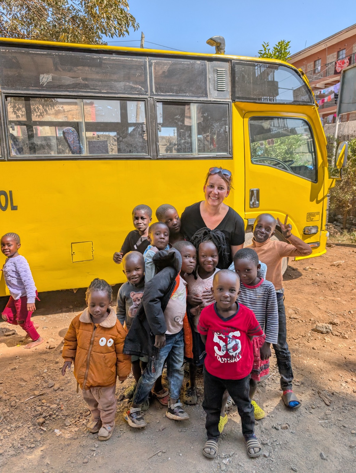 A group of kids with an adult in front of a yellow school bus in Kenya.