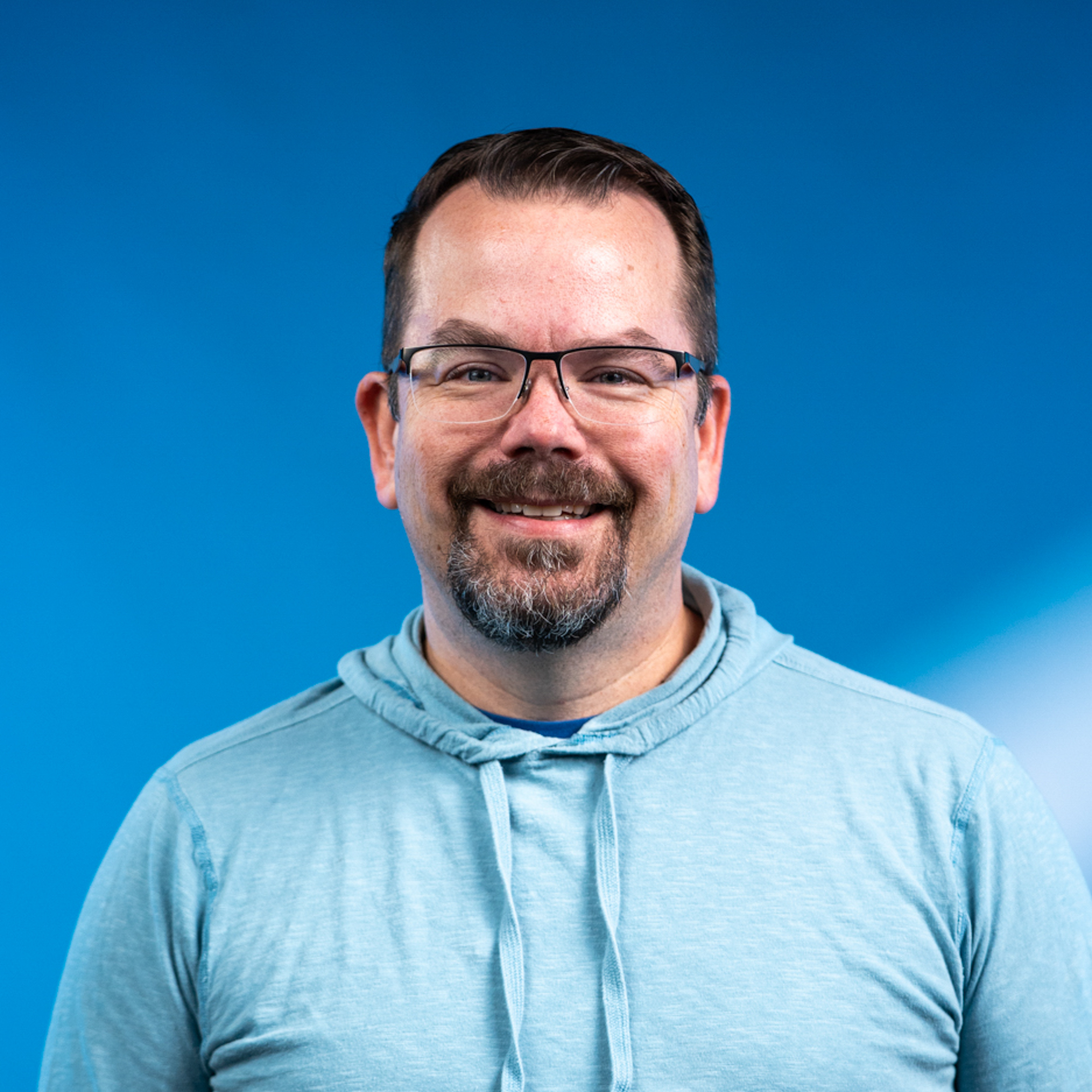 A older white man with brown hair and a beard with rectangle glasses.