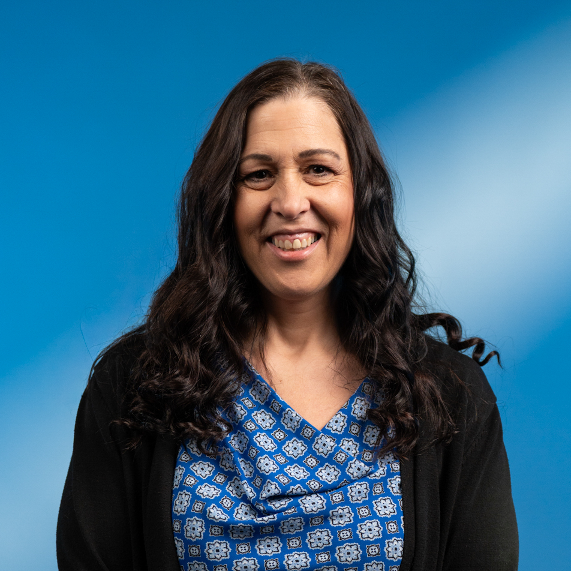 A middle-aged white woman with wavy dark brown hair and brown eyes.