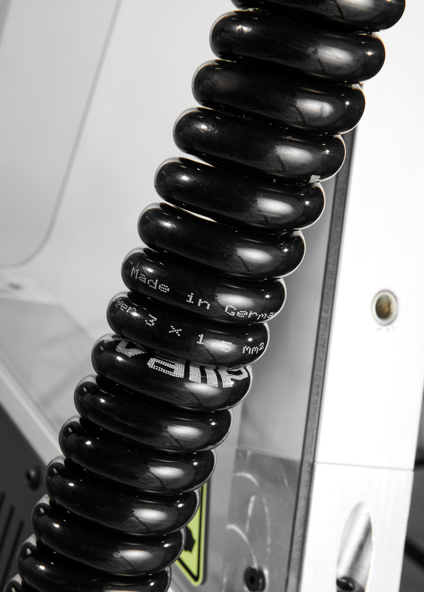 Close-up of a black coiled cable with white text reading 'Made in Germany' wrapped around a metallic surface.