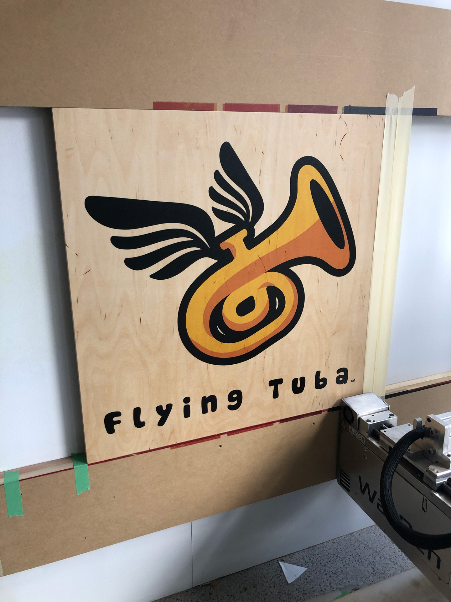 Wooden panel with a colorful illustration of a tuba with wings and the text 'Flying Tuba' below.