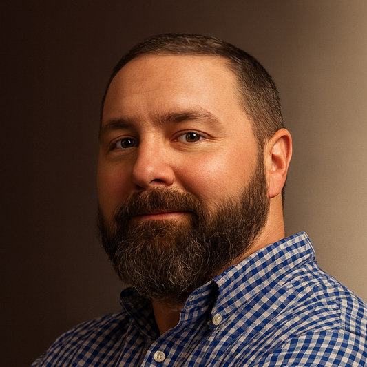 Brian Mallan Bearded man wearing blue and white checkered shirt against a gradient brown background.
