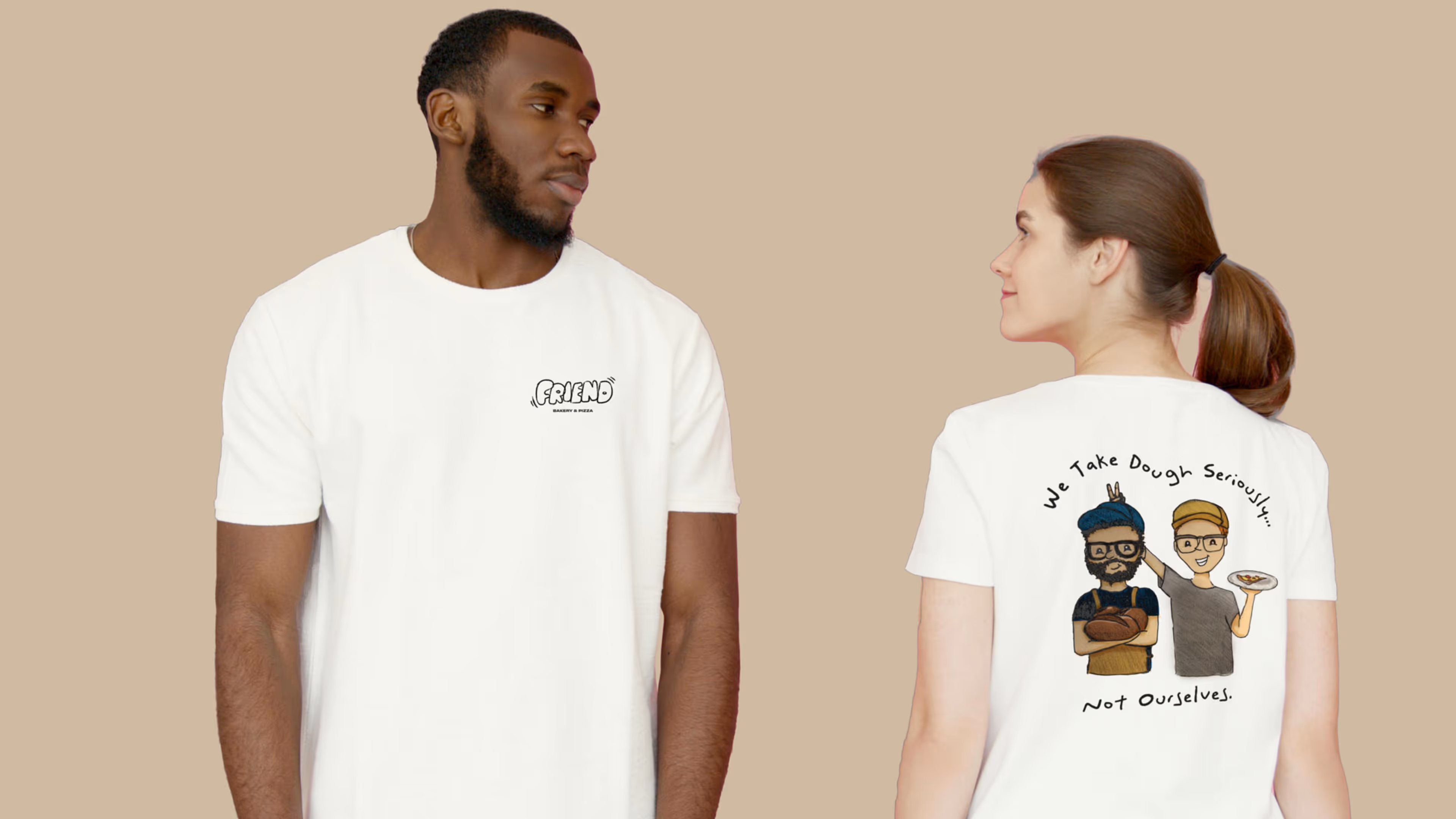 Man and woman wearing white t-shirts with bakery-themed prints, woman’s back shows cartoon of two bakers with text 'We Take Dough Seriously... Not Ourselves.'