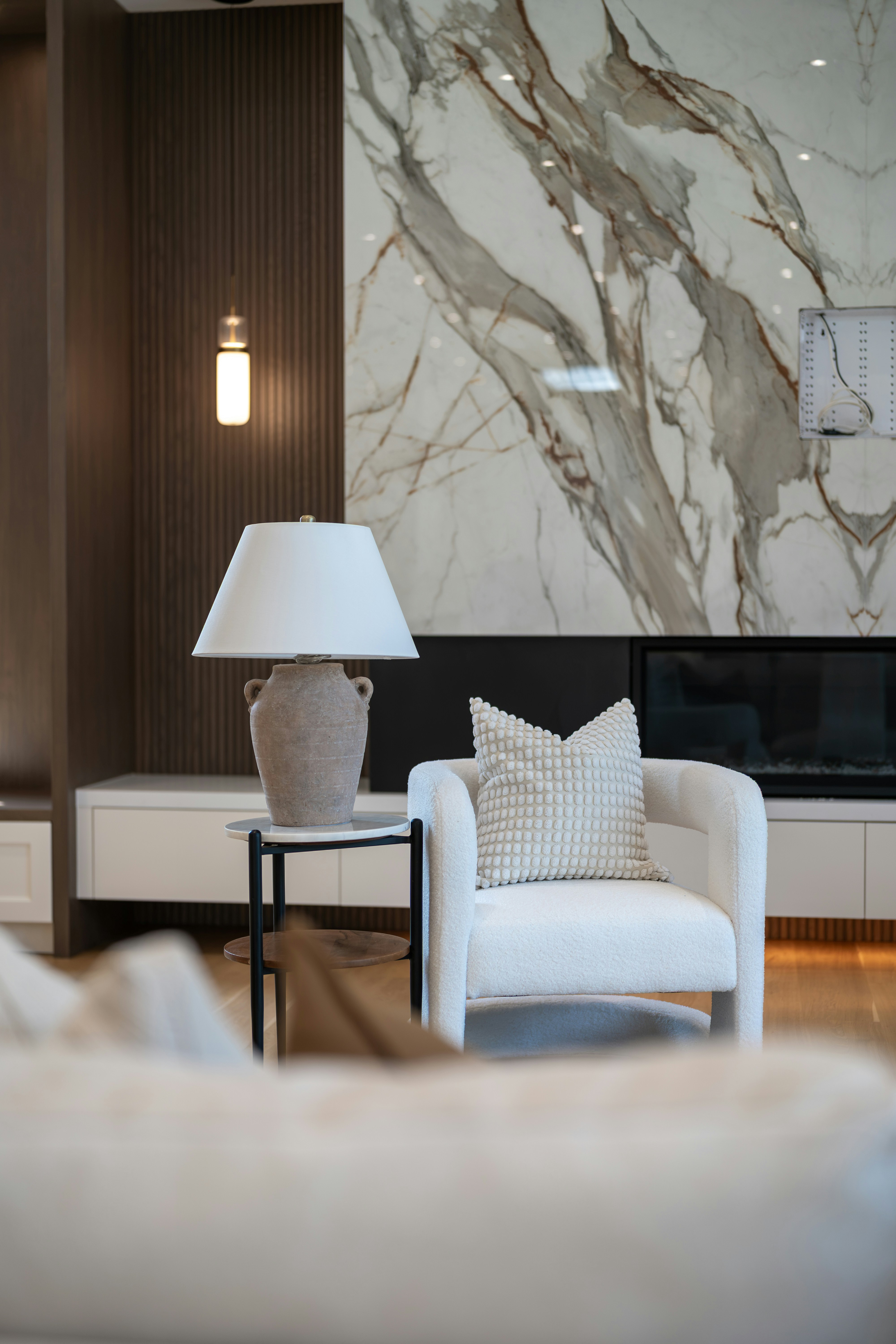 Detail of a white accent chair beside a marble fireplace wall