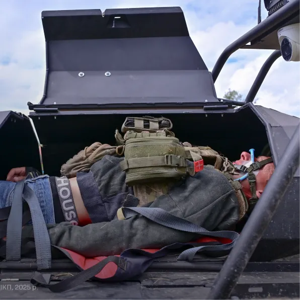 Person wearing tactical gear lying inside an open black armored vehicle compartment.