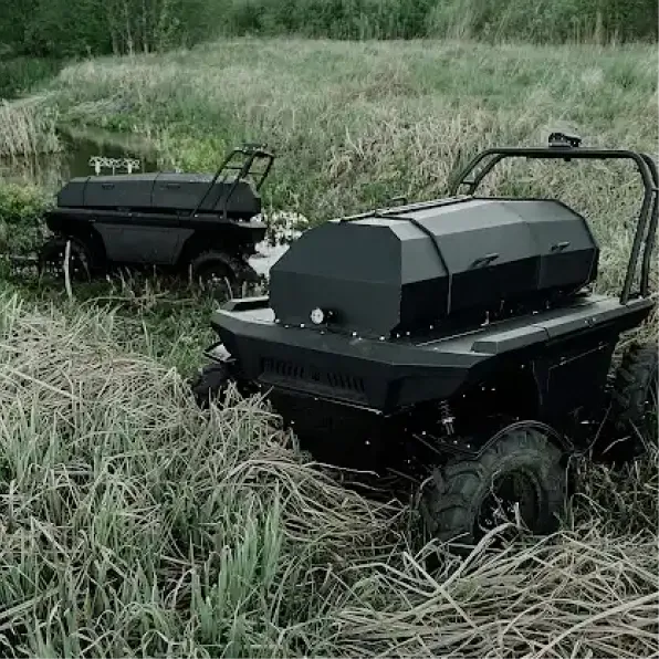 Two black autonomous off-road vehicles navigating through tall grass near a small body of water in a natural, green environment.
