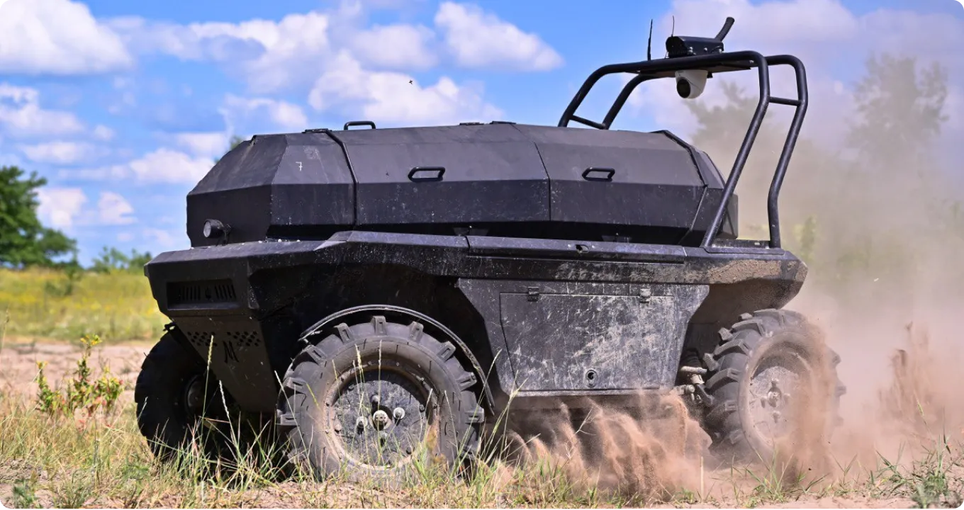 Black autonomous all-terrain vehicle kicking up dust while driving on a grassy field under a blue sky with clouds.