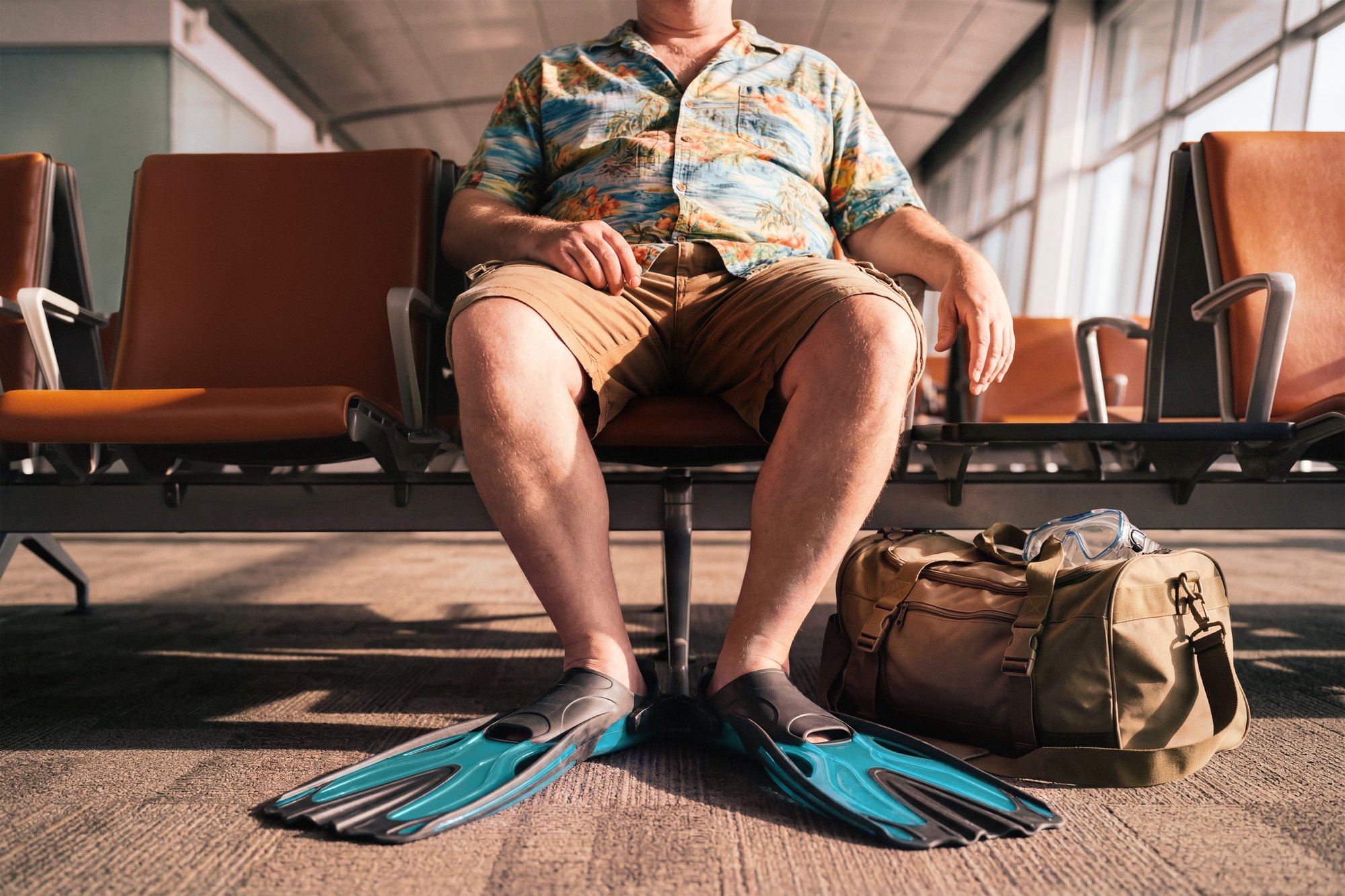 The Reef: a traveller in a Hawaiian shirt and blue dive fins waiting at an airport gate with a duffel bag, shown from the knees down - AI-generated image by Matter Studio for Zurich Travel Guard
