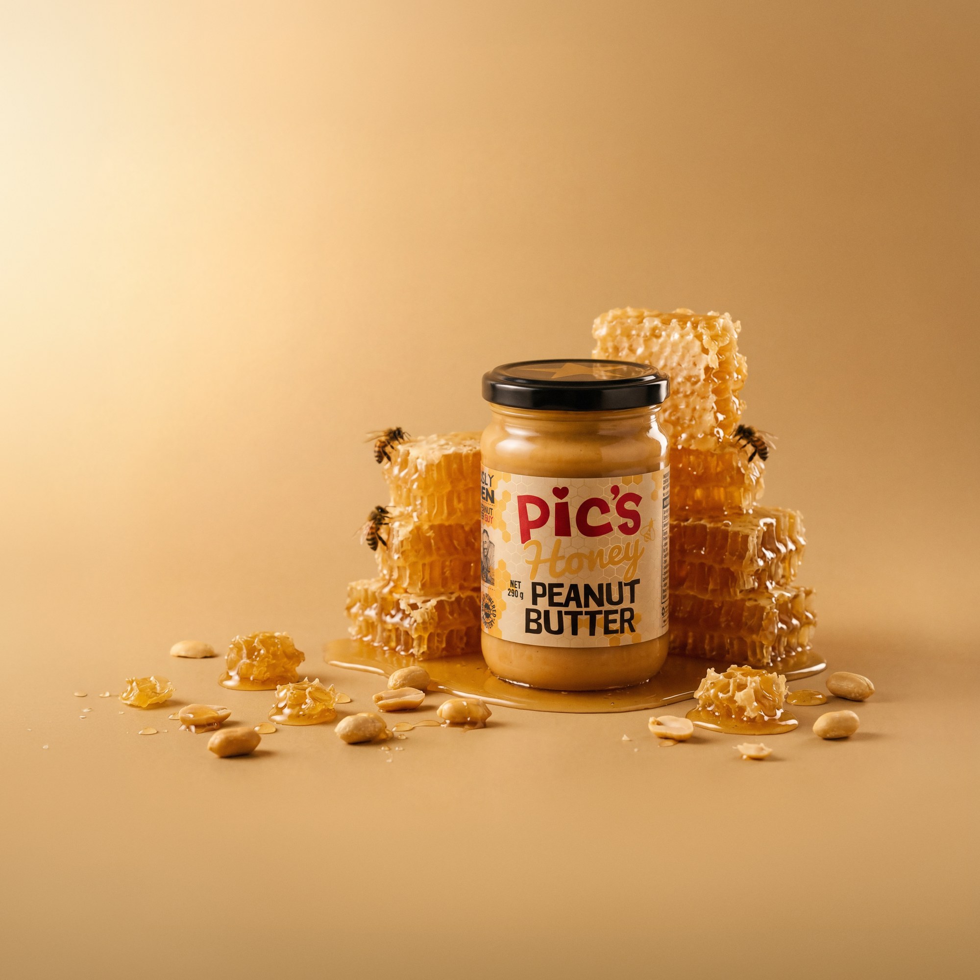 Pic's Honey Peanut Butter jar surrounded by stacked raw honeycomb, bees and scattered peanuts on a warm amber background - product image built by Matter Studio from a pre-production jar