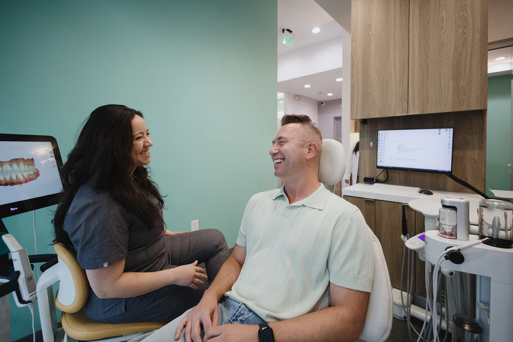 Smiling dentist talking with a male patient seated in a dental chair in a modern clinic.