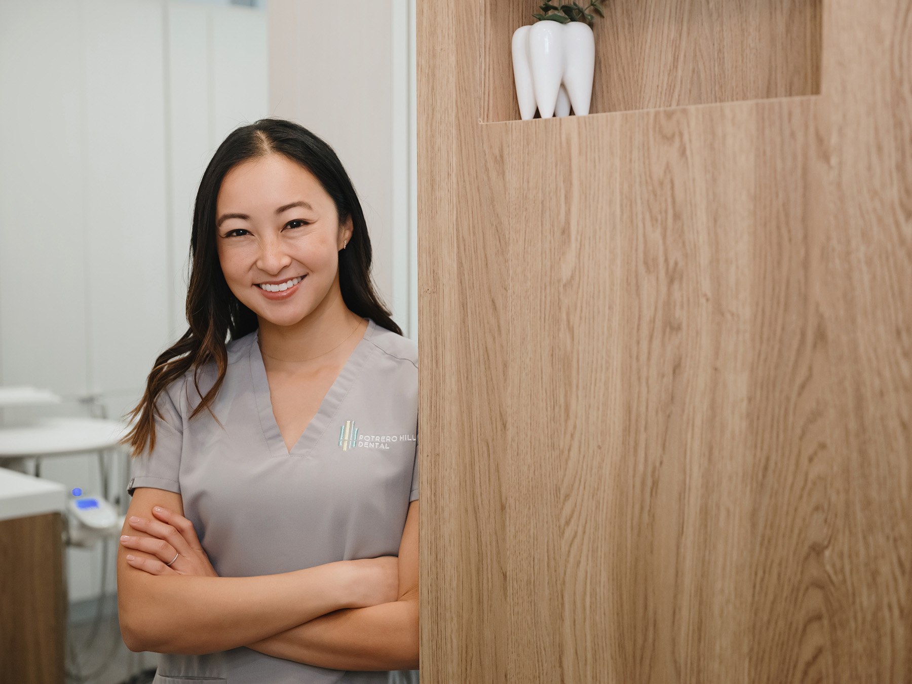 Smiling female dental professional standing with arms crossed in a modern dental office.