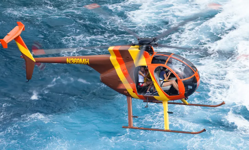 Red and yellow MD 500 helicopter flying along Oahu coastline