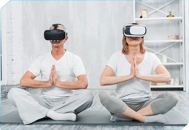 Senior man and woman sitting cross-legged on yoga mats, meditating with hands in prayer position while wearing virtual reality headsets.